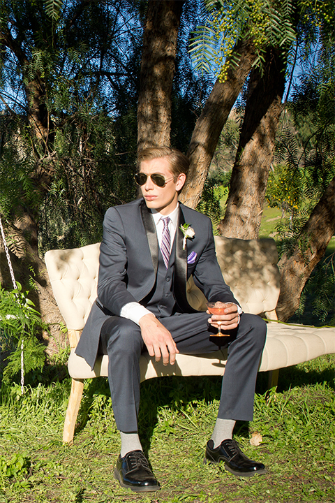 San diego outdoor woodland wedding shoot groom navy blue shawl lapel tuxedo with matching vest and white dress shirt and long pink striped tie and white floral boutonniere sitting on vintage bench wearing sunglasses