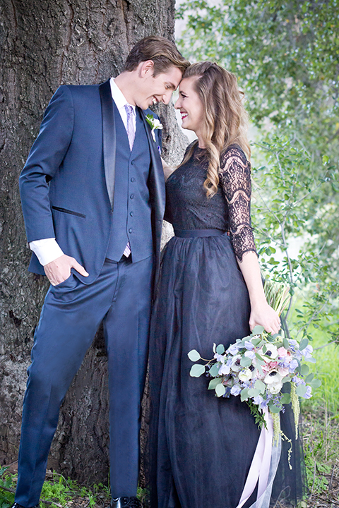 San diego outdoor woodland wedding shoot bride black chiffon gown with long lace sleeves and high lace neckline holding white floral bridal bouquet with groom navy blue shawl lapel tuxedo with matching vest and white dress shirt with a long pink striped tie and white floral boutonniere standing next to pony wedding photo idea