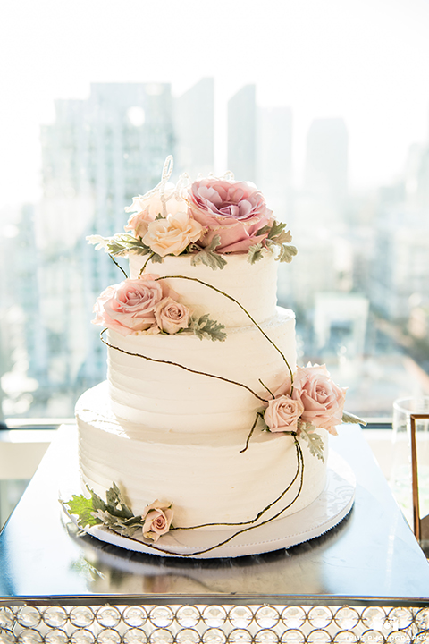 San diego outdoor wedding at the ultimate skybox reception table set up white table linen with gold and white chairs and pink napkin decor with white and blush pink flower centerpiece decor and table numbers with wedding cake three tier white cake with blush pink flower decor on top and on sides