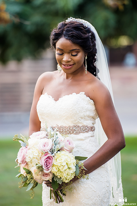 San diego outdoor wedding at ultimate skybox bride form fitting strapless lace gown with a sweetheart neckline and crystal belt with long veil holding white floral bridal bouquet