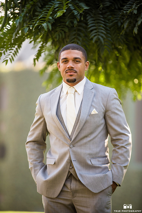 San diego outdoor wedding at ultimate skybox groom heather grey notch lapel suit with a white dress shirt and matching vest with a long white tie and white pocket square with a white floral boutonniere