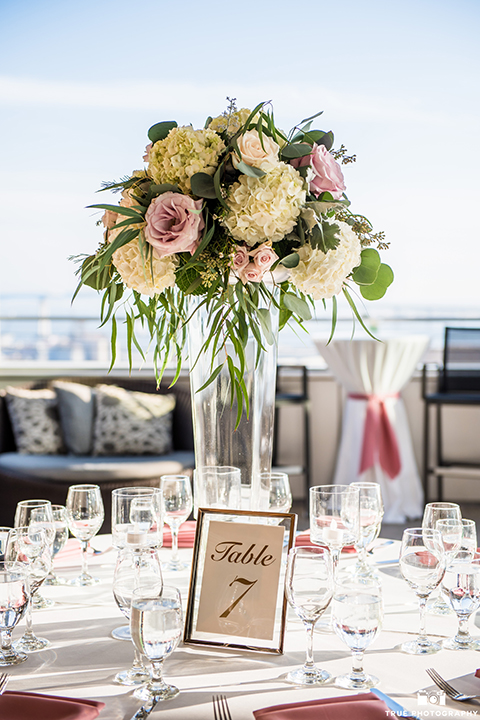 San diego outdoor wedding at the ultimate skybox reception table set up white table linen with gold and white chairs and pink napkin decor with white and blush pink flower centerpiece decor and table numbers