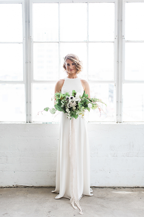 Downtown los angeles wedding shoot at fd photo studio bride form fitting simple gown with a high halter neckline holding white and green floral bridal bouquet