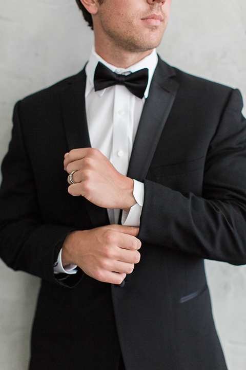 Downtown los angeles wedding shoot at fd photo studio groom black notch lapel tuxedo by michael kors with a white dress shirt and black bow tie holding sleeve