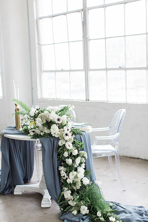 Downtown los angeles wedding shoot at fd photo studio table set up with grey table linen and white and green flower decor with clear ghost chairs and white and grey place settings with white candle decor and piano
