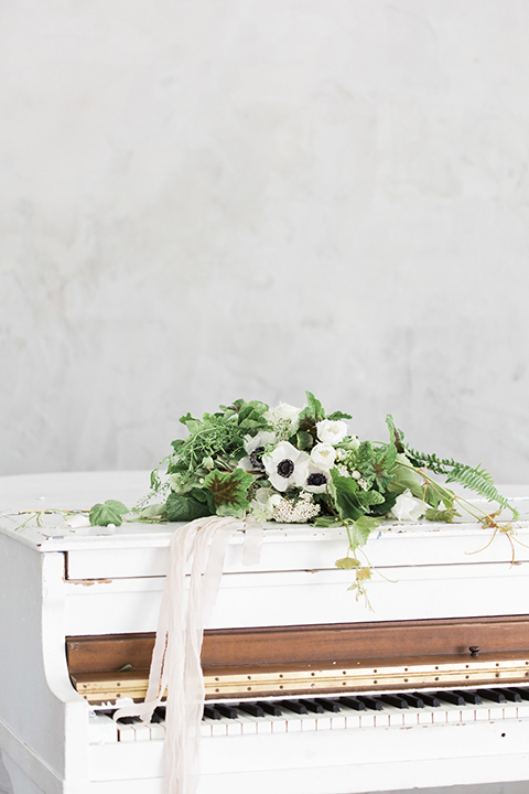 Downtown los angeles wedding shoot at fd photo studio table set up with grey table linen and white and green flower decor with clear ghost chairs and white and grey place settings with white candle decor and piano