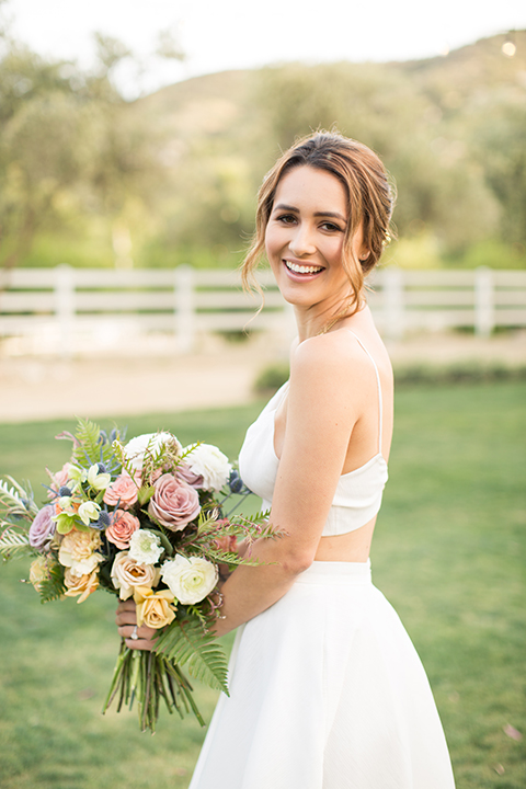Los angeles outdoor wedding at brookview ranch bride two piece wedding dress with tulle skirt and crop top bodice with thin straps and a sweetheart neckline holding white and pink floral bridal bouquet close up