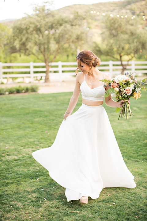 Los angeles outdoor wedding at brookview ranch bride two piece wedding dress with tulle skirt and crop top bodice with thin straps and a sweetheart neckline holding white and pink floral bridal bouquet