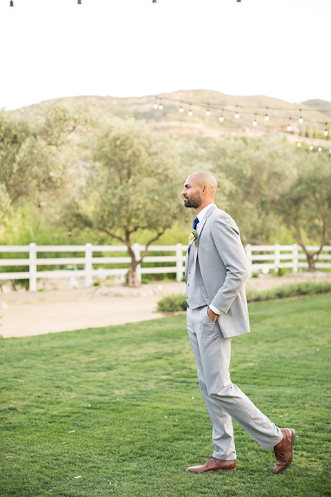 Los angeles outdoor wedding at brookview ranch groom heather grey notch lapel suit with a matching vest and white dress shirt and long blue tie and white floral boutonniere standing