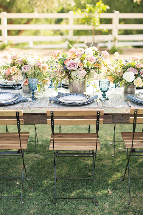 Los angeles outdoor wedding at brookview ranch table set up dark brown wood table with matching wood chairs with blue place settings and blue glasses with white and pink flower decor with gold vases and greenery decor