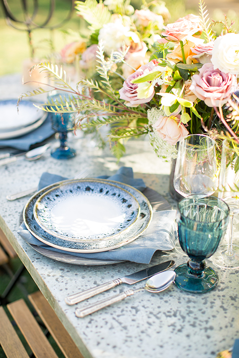 Los angeles outdoor wedding at brookview ranch table set up dark brown wood table with matching wood chairs with blue place settings and blue glasses with white and pink flower decor with gold vases and greenery decor