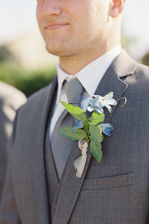 San diego outdoor rustic wedding groom grey notch lapel suit with a white dress shirt and matching vest with a long grey tie and blue floral boutonniere close up